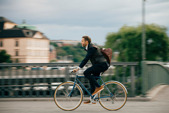 Full length of confident businessman riding bicycle on bridge