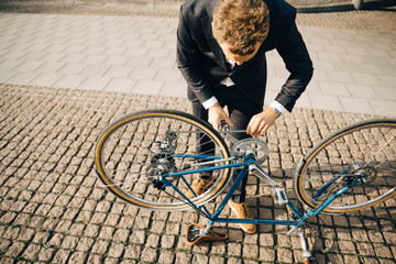High angle view of businessman repairing bicycle chain on cobbled footpath in city