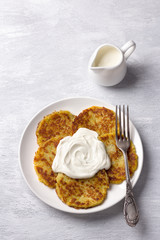 Traditional latkes fritters with sour cream on a light gray textured background, top view