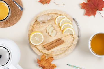 Close up photo of wooden platter with lemon, ginger and cinnamon sticks. Near bowl of honey, teapot, a cup of tea and thermometer. Natural remedies for flu and colds. Winter season concept. Flat lay.