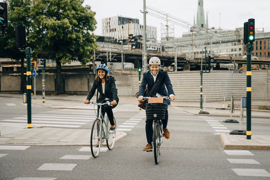 Smiling businessman and businesswoman riding bicycles on road in city