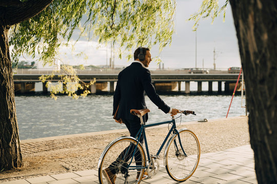 Businessman walking with bicycle on footpath by canal in city - Powered by Adobe