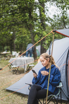 Teenage girl using mobile phone while having coffee at campsite