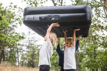 Siblings carrying inflatable mattress walking at camping site