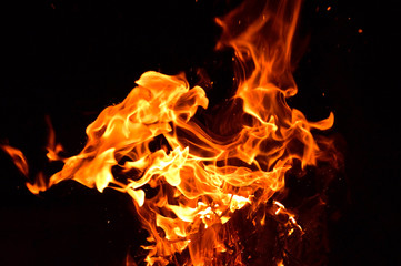in the photo of a dark night, a yellow-red flame burns, firewood is visible from below