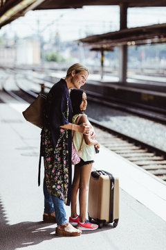 Mother with daughter with luggage waiting for train on railroad station platform