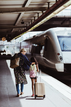 Rear view of mother and daughter walking on railroad station platform
