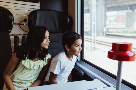 Siblings looking through window while traveling together in train