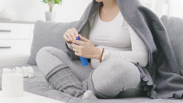 Pregnant woman catching cold, flu, virus, sitting at home on a couch, using tablet in the cup and being sick.
