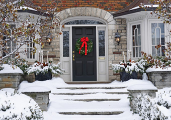 Front door of snow covered house with Christmas wreath