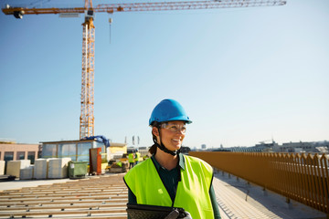 Smiling female engineer in reflective clothing with digital tablet at construction site against clear sky