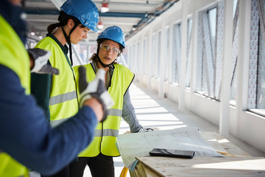 Female and male engineers discussing over blueprints at construction site