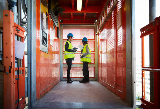 Side view of engineers talking with each other in freight elevator at construction site