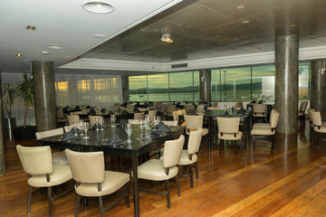 Luxurious party room with various tables, plates, cutlery and wine glasses. Windows overlooking the sea and sunset. Hall for events, parties, celebrations with beautiful view.