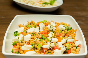 Closeup of Chickpea Salad with Tomatoes, Brocolis and Buffalo Cheese on a Foursquare Ceramic Platter on Wooden Table. Healthy and tasty food. Selective focus.