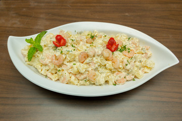 Close up of potato salad with shrimp and mayonnaise. Delicious, nutritious and healthy meal in a white ceramic serving dish on the wooden table. Selective focus