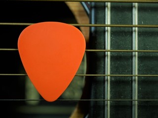 Close up of clear orange guitar pick plecturm resting on guitar strings and fret board background