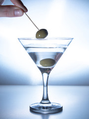 a man's hand pulls an olive on a skewer from a glass of water