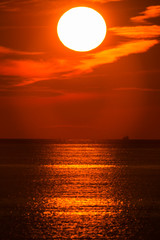 水平線の上に昇る朝の太陽と横切る船の影