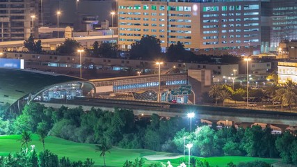 Metro station services both the Dubai Internet City and Dubai Media City districts of Dubai, as well as Golf Club night timelapse. Aerial view from Greens district with illuminated buildings on a