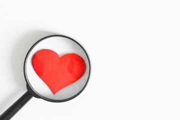 Red heart under a magnifying glass on a white background. Verification, confirmation and...