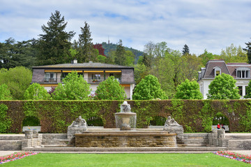 Beautiful public park in a European city with an antique fountain and green bushes, with text space