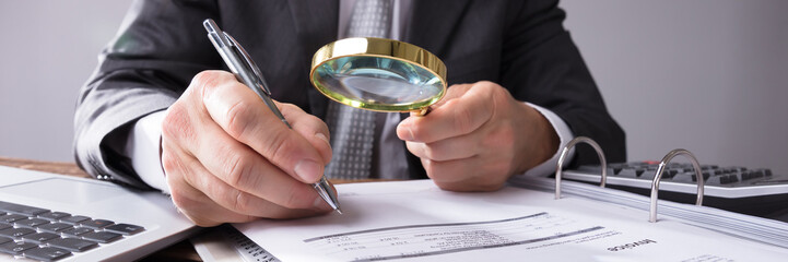 Businessperson Looking At Receipts Through Magnifying Glass