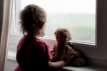 Kleines Kind mit Teddy schaut aus dem Fenster