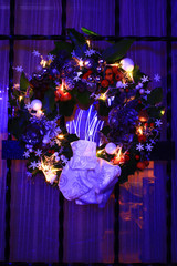 Advent wreath hanging on a house door. Christmas decoration with a light garland, with stars, mistletoe, balls and snowman. Colorful red and blue bokeh background.