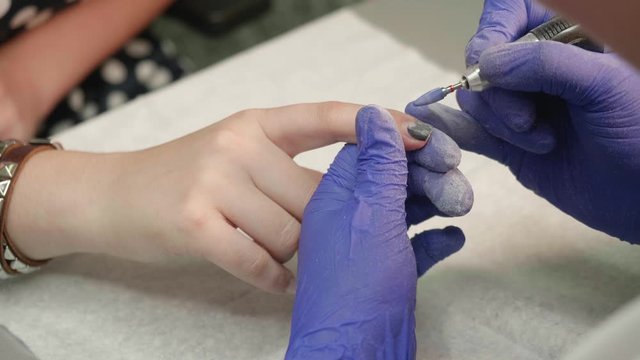 Hands of manicurist removing old nail jel polish with manicure machine from hands of client.