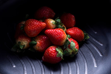 A small amount of strawberries are placed in a black pan.