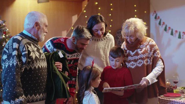 Happy family reunion. Beautiful married couple with kids and grandparents reading a book fairytale opening presents enjoying celebration together.