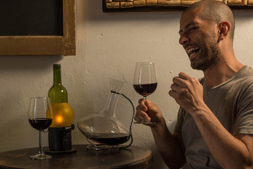 Man smiling and holding a wine glass at a table with bottles and a old lamp