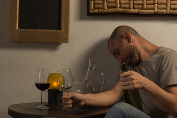 Drunk man holding a cup and a bottle on a table
