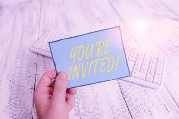 Writing note showing You Re Invited. Business concept for make a polite friendly request to someone go somewhere Man holding colorful reminder square shaped paper wood floor