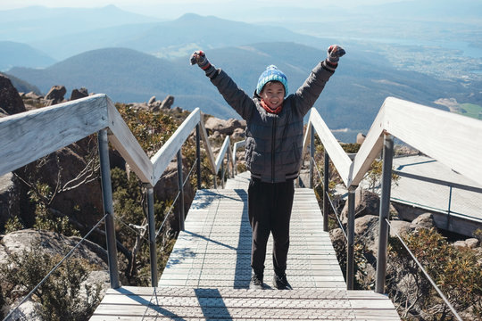 Mixed race Asian tween boy standing with hand up on top of the mountain, Preteen travel concept, accomplishment and Achievement for teenager