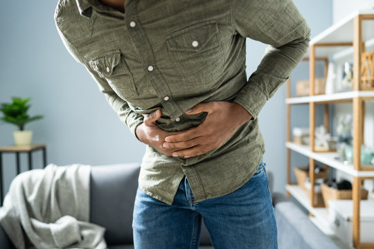 Man With Stomach Ache Standing Near Couch At Home