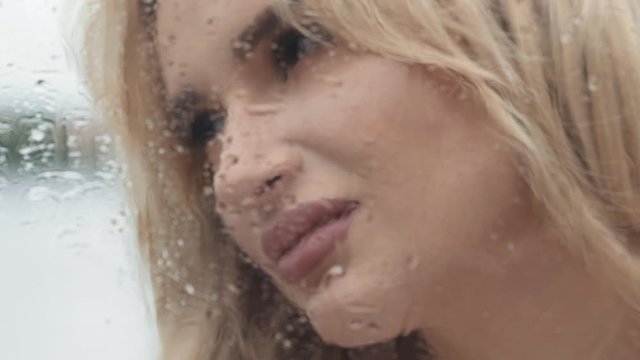 Passionate portrait of blonde touches wet from rain window