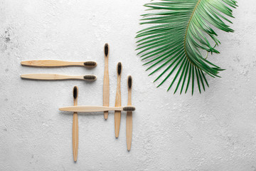 Zero waste, biodegradable bamboo toothbrush on a gray stone concrete countertop with a green palm leaf on the side. The concept of save the planet, ecology, eco