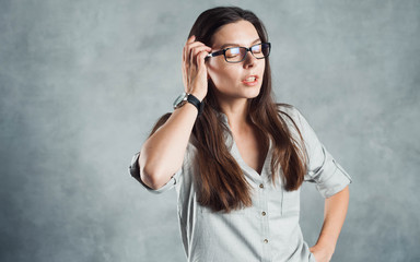 Young successful confident woman in a gray shirt against a textured gray wall.