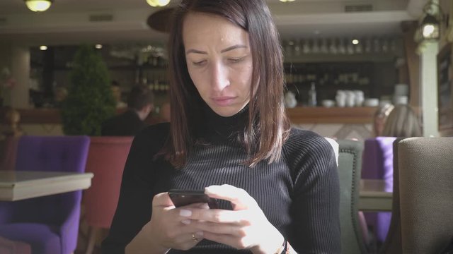 Young wonam use mobile phone while sitting in comfortable coffee shop during work break, charming happy female reading fashion news on cell telephone during breakfast in restaurant.