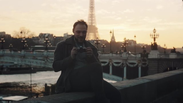 Cheerful romantic tourist man taking a photo, smiling on autumn Seine sunset river bank in dreamy Paris slow motion.