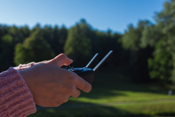 Female hands with a neat manicure hold a drone control panel with drumbo antennas and a larger display. Outdor.