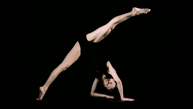 A flexible female dancer stretches out against an infinite black background.