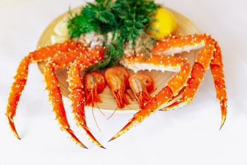 Shrimp, crab, lemon and greens on a plate on a white background.