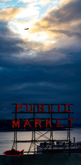 PIKE PLACE MARKET SUNSET VIEW OF PUGET SOUND WATERS ABD ALKI BEACH WITH JET AIRCRAFT SILHOUETTED IN SUNLIT CLOUDY SKY