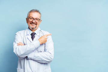 Cheerful mature doctor posing and smiling at camera, healthcare and medicine. Isolate on blue...
