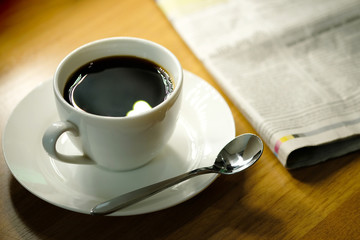 Cup of coffee hot on the desk has a newspaper and a tablet. at office