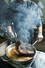 The chef works in the kitchen of the restaurant. Fresh meat roasted in a large frying pan. Restaurant kitchen background
