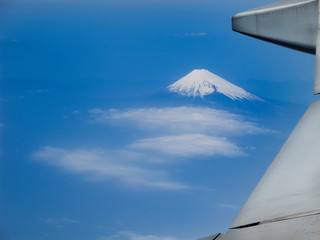 wing of airplane flying above clouds with volcano mountain